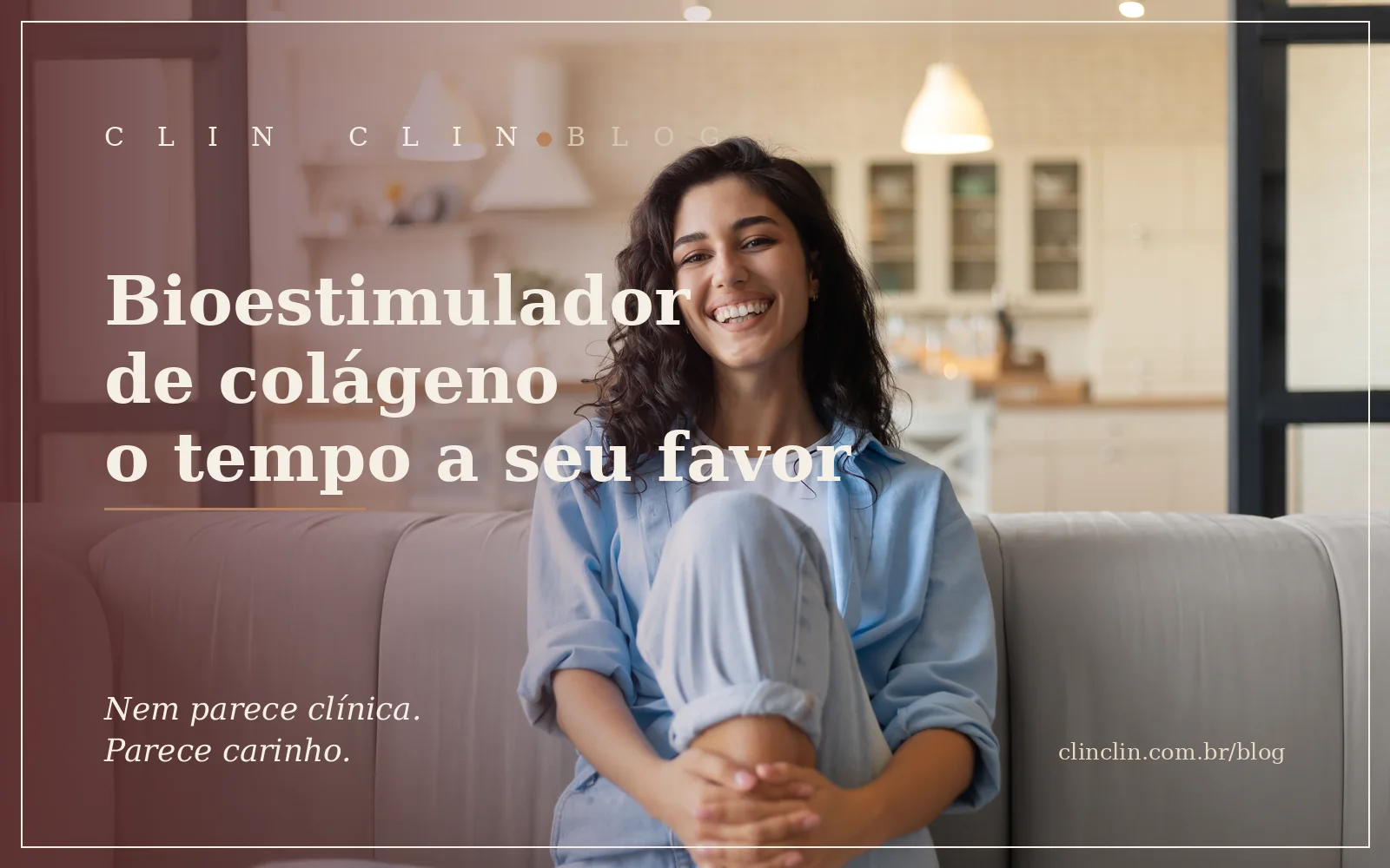 Mulher jovem sorrindo, sentada no sofá de casa, em luz natural suave, com a cozinha desfocada ao fundo