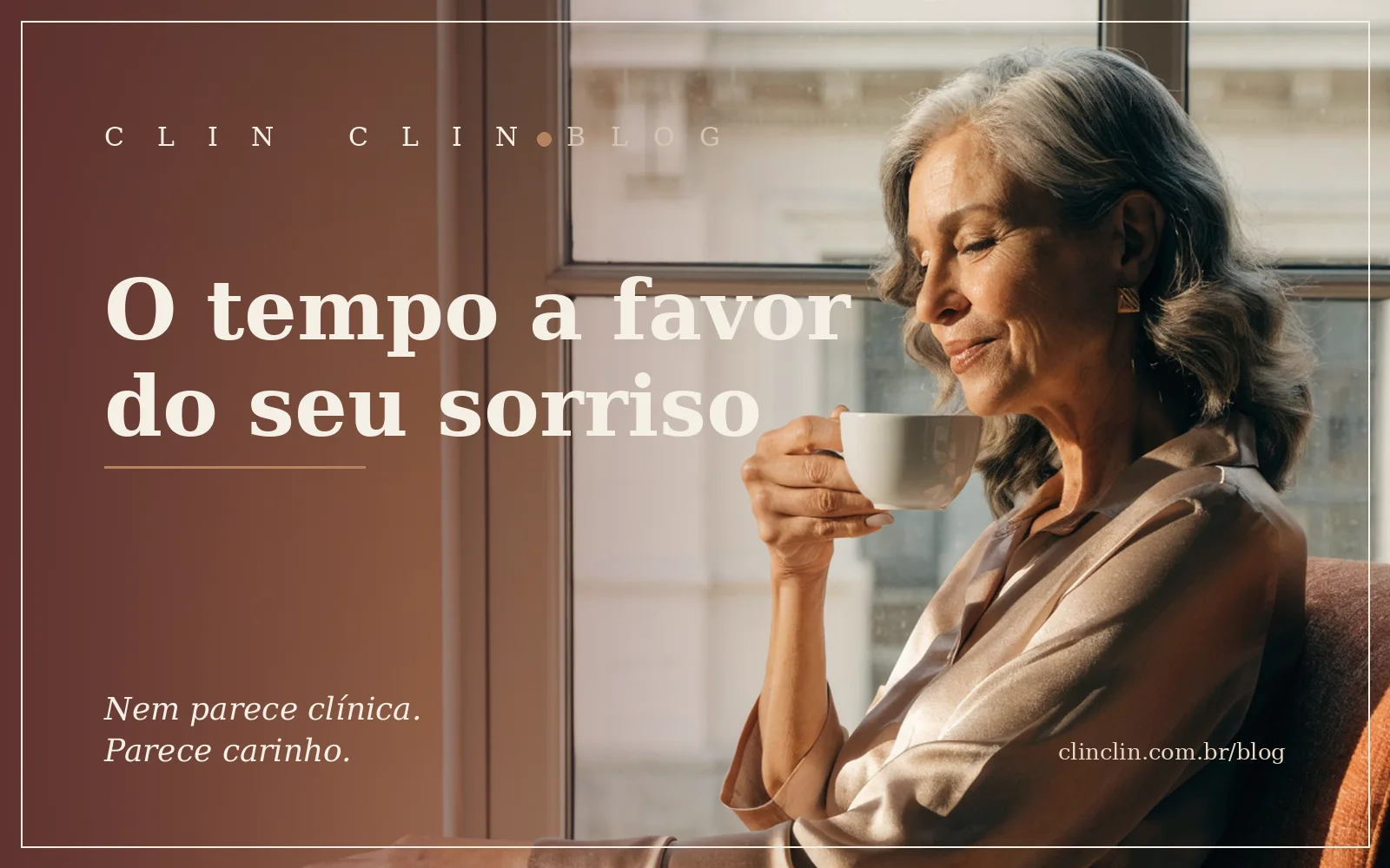 Mulher branca de uns cinquenta anos, cabelos grisalhos soltos, sentada perto da janela numa manhã de luz quente, sorrindo enquanto segura uma xícara de café.