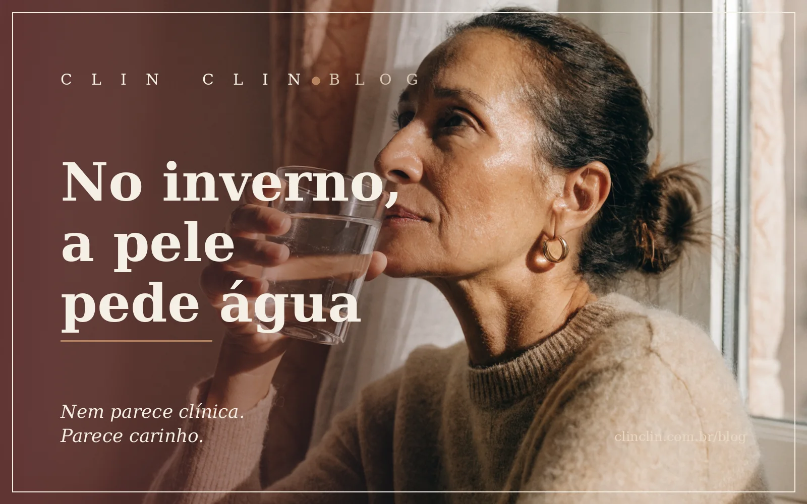 Mulher madura de roupa de tricô junto à janela, copo de água nas mãos, na luz clara de uma manhã de inverno, pele serena e descansada