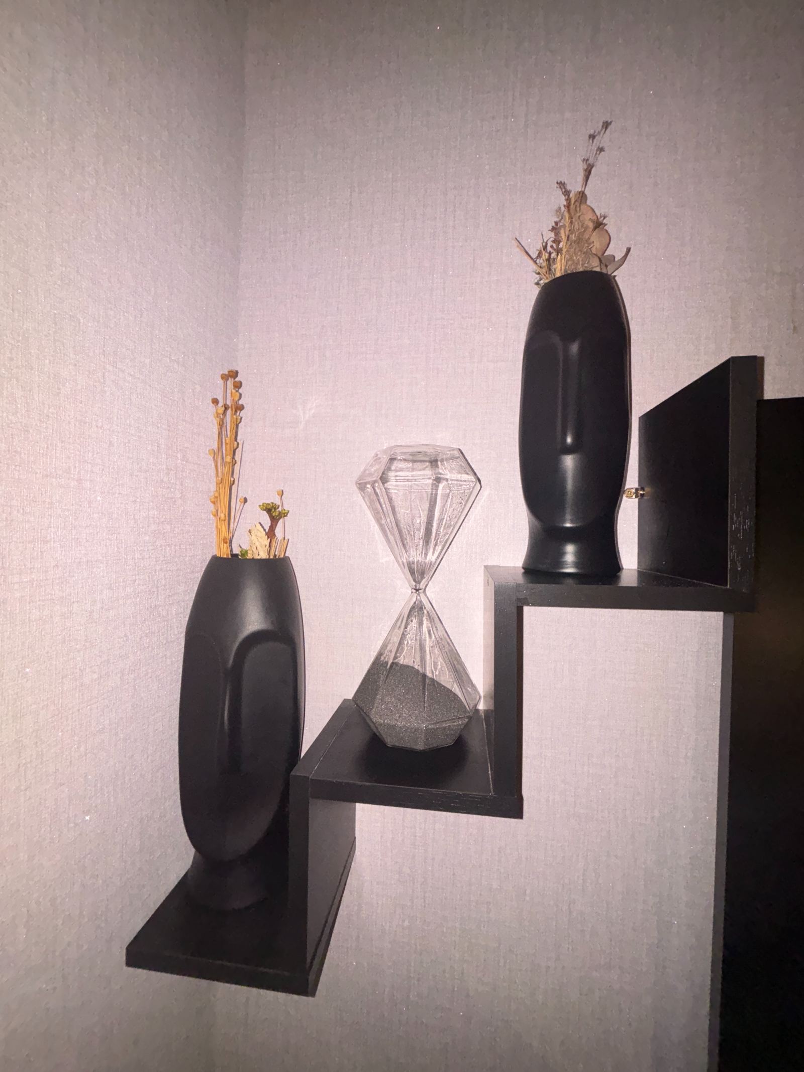 Vasos pretos com flores secas e ampulheta de vidro em prateleira escalonada