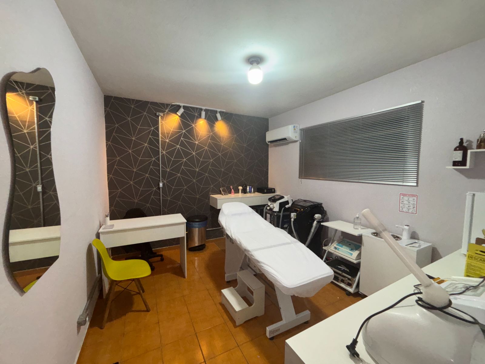 Sala de estética: maca branca, aparelhos de laser e parede geométrica